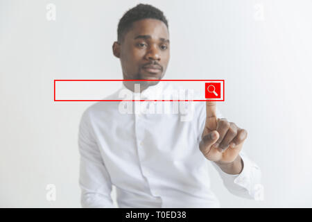 Handsome businessman pointing his finger to the camera and slicking virtual button, finger is in focus while his face is out of focus. Shallow depth of field. Young african american guy interacts with empty search bar. Negative space to insert your text. Stock Photo