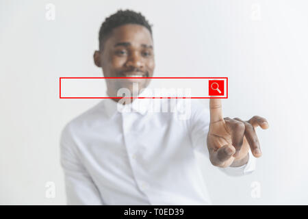 Handsome businessman pointing his finger to the camera and slicking virtual button, finger is in focus while his face is out of focus. Shallow depth of field. Young african american guy interacts with empty search bar. Negative space to insert your text. Stock Photo