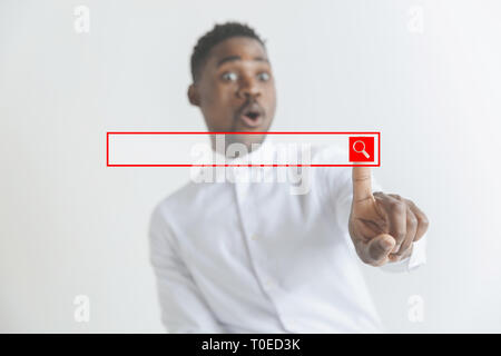 Handsome businessman pointing his finger to the camera and slicking virtual button, finger is in focus while his face is out of focus. Shallow depth of field. Young african american guy interacts with empty search bar. Negative space to insert your text. Stock Photo
