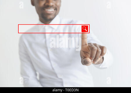 Handsome businessman pointing his finger to the camera and slicking virtual button, finger is in focus while his face is out of focus. Shallow depth of field. Young african american guy interacts with empty search bar. Negative space to insert your text. Stock Photo