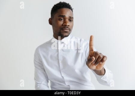 Handsome businessman pointing his finger to the camera and slicking virtual image or text, finger is in focus while his face is out of focus. Shallow depth of field. Young african american guy interacts with empty space. Negative space to insert your text or image. Stock Photo