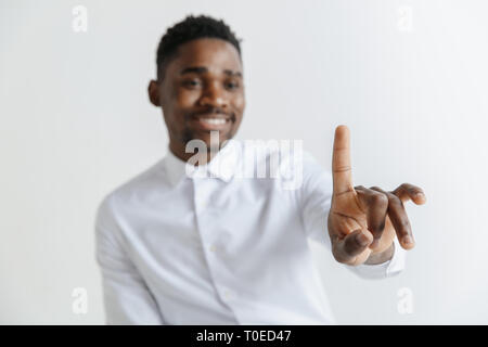 Handsome businessman pointing his finger to the camera and slicking virtual image or text, finger is in focus while his face is out of focus. Shallow depth of field. Young african american guy interacts with empty space. Negative space to insert your text or image. Stock Photo