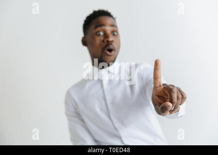 Handsome businessman pointing his finger to the camera and slicking virtual image or text, finger is in focus while his face is out of focus. Shallow depth of field. Young african american guy interacts with empty space. Negative space to insert your text or image. Stock Photo