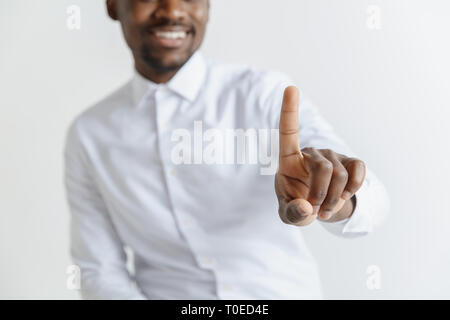 Handsome businessman pointing his finger to the camera and slicking virtual image or text, finger is in focus while his face is out of focus. Shallow depth of field. Young african american guy interacts with empty space. Negative space to insert your text or image. Stock Photo