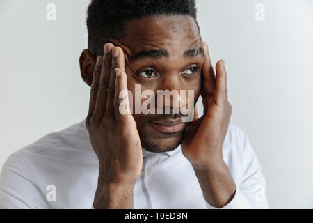 Stressed young african american man feel pain and having terrible strong headache concept. Tired upset black guy massaging temples and suffering from migraine isolated on grey studio blank background Stock Photo