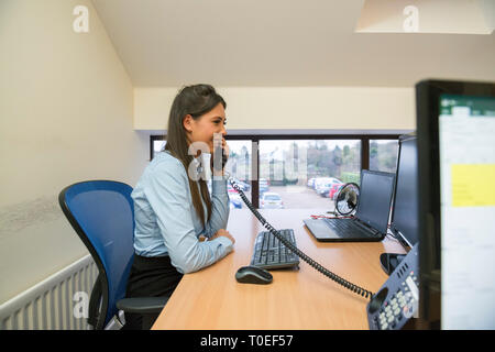 woman on the phone while sat at her desk in an office environment making a phone call on the landline phone. Stock Photo