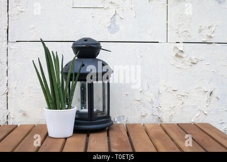 Old glass lantern with candle and Sansevieria cylindrica (cylindrical snake plant) potted flower on wooden table by white background. Home decor with  Stock Photo