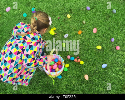 Girl from the back on early easter egg hunt collecting colorful eggs from the green grass Stock Photo