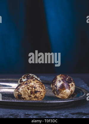 Several eggs of quail on a silver, oval tray on a blue table. Stock Photo