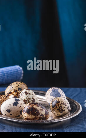 Several eggs of quail on a silver, oval tray on a blue table. Stock Photo