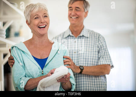 Affectionate mature couple share a laugh together as they dry the dishes. Stock Photo