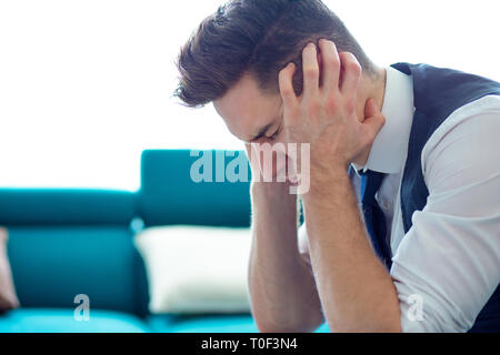 Stressed young business man with hands on head feeling worried and looking down sitting on couch Stock Photo