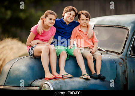 Portrait of three young siblings sitting together on an old car. Stock Photo