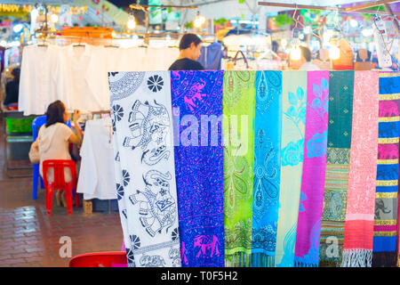 Colorful shawls and white shirts on stall, at night street market, Chiang Mai, Thailand Stock Photo