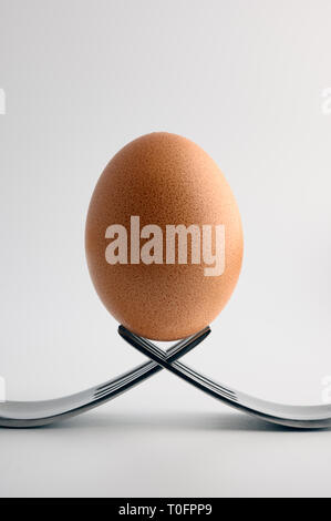 Egg in balance on two forks on white background Stock Photo