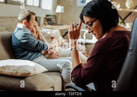 Thoughtful dark-haired woman leaning on her hand while analyzing the situation Stock Photo