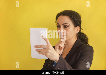 Beautiful young business woman, with pigtail, black jacket, isolated on a background, looking at her tablet. Woman analyzing data Stock Photo