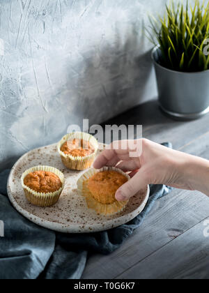 Homemade muffins on craft plate over gray wooden table. Hand hold carrot cupcake. Copy space. Toned image in scandinavian style. Stock Photo