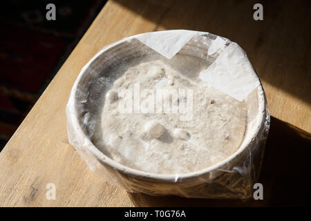 Sourdough bread proofing in a basket covered with plastic foil. Homemade baking concept. Stock Photo