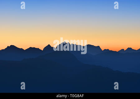 Silhouettes of mountain ranges at dawn with orange and blue sky. Beautiful morning mood in the Allgaeu Alps. Border region of Germany and Austria. Stock Photo