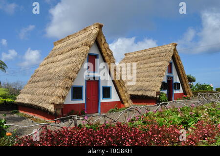 Typical stone houses, painted red, white and blue, with triangular shaped straw thatched roof in the village of Santana / Santa Ana, Madeira, Portugal Stock Photo