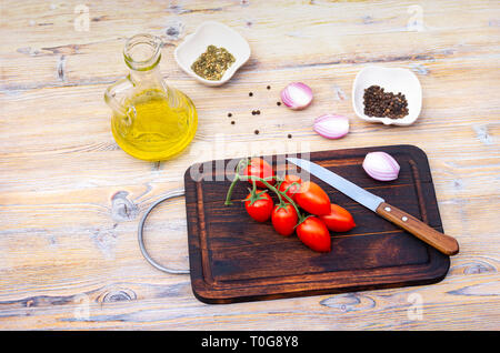 Cherry tomatoes on a branch, vegetable oil and spices on a wooden background, top view Stock Photo