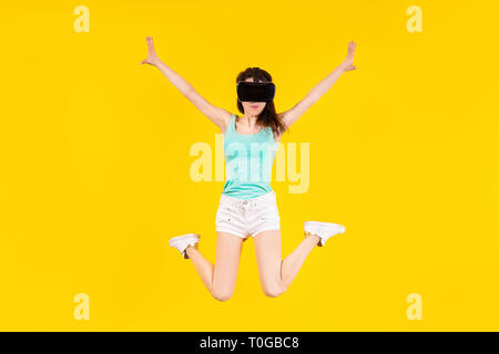 girl in VR glasses of virtual reality is jumping on a yellow background Stock Photo
