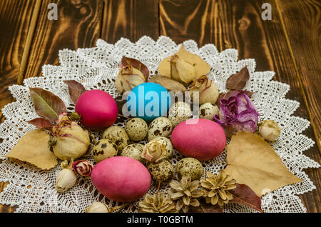 White openwork napkin with Easter eggs and quail eggs among dry rose buds and dry leaves on dark polished boards Stock Photo