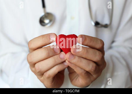Cardiology and health care, doctor holding red knitted heart in hands. Concept of cardiologist, blood donation, treatment of heart disease in clinic Stock Photo