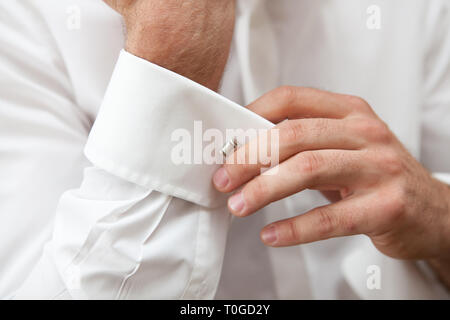 An elegant man is getting dressed in white shirt with cufflinks, securing them in place. Stock Photo