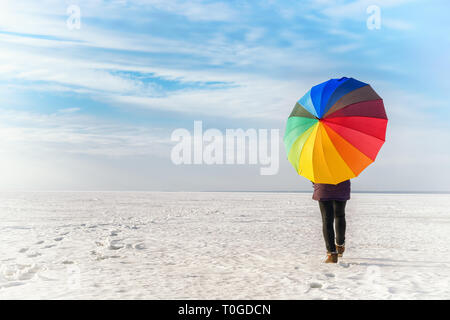 Woman with rainbow colored umbrella walking on frozen sea. Bright colored winter landscape Stock Photo