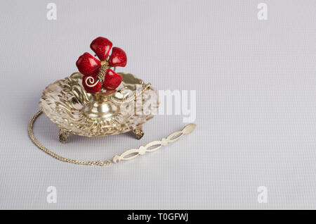 Traditional silver 'Attardani' or perfume container on white coloured background and artificial red rose flower also made from silver. Stock Photo