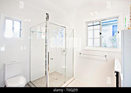 Modern clean fresh white bathroom with glass shower cubicle and toilet lit by daylight from a large window Stock Photo
