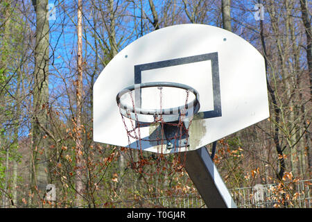 Old run down and rusty basketball basket on play ground surrounded by forest Stock Photo