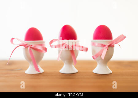 three pink colored easter eggs in holders on table Stock Photo