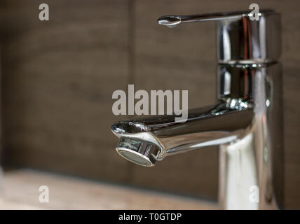 A close up shot chrome mixer tap in a bathroom against dark tile background Stock Photo