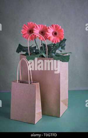Coral gerbera daisy flowers and craft papper shopping bags on green paper background, Springtime sale concept image with copy-space Stock Photo