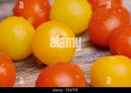 yellow and red cherry tomatoes on a wooden surface, water drops on it, color macro picture Stock Photo