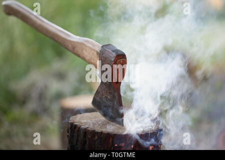 Axe in tree stump and smoke from campfire Stock Photo