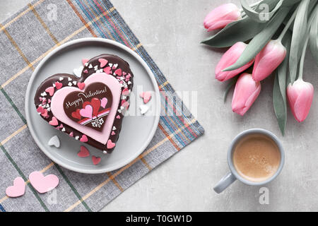 Valentine heart cake with chocolate, sugar decorations and greeting text 'Happy Valeitine' on grey stone table top with pink tulips Stock Photo