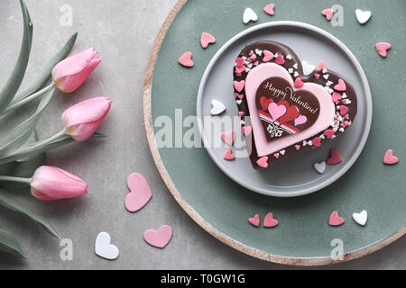 Valentine heart cake with chocolate, sugar decorations and text 'Happy Valeitine' and a bunch of pink tulips. Top view on light background. Stock Photo