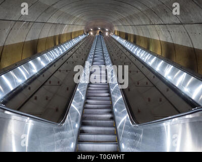 Washington DC, United States - 3 March 2019. Long escalator leading up from Adams Morgan Metro station through concrete tunnel illuminated in cold, me Stock Photo