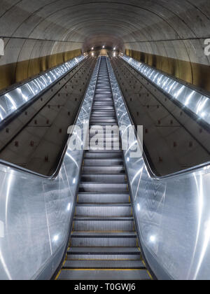 Washington DC, United States - 3 March 2019. Long escalator leading up from Adams Morgan Metro station through concrete tunnel illuminated in cold, me Stock Photo