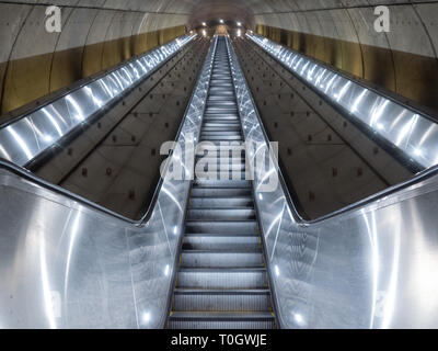 Washington DC, United States - 3 March 2019. Long escalator leading up from Adams Morgan Metro station through concrete tunnel illuminated in cold, me Stock Photo
