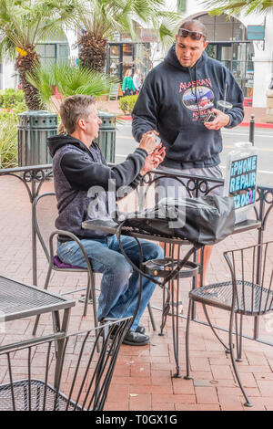An iPhone repairman who set up shop on the sidewalk patio of a local coffee shop with a homemade sign stating 'iPhone Repair' and his phone number, gi Stock Photo