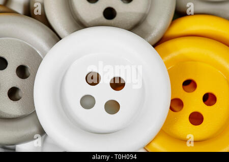 Close up of a large white button sitting on yellow and grey buttons with shallow depth of field Stock Photo