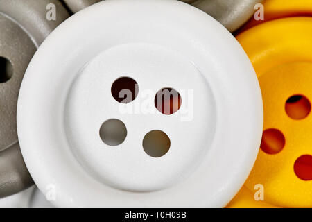 Close up of a large white button sitting on yellow and grey buttons with shallow depth of field Stock Photo