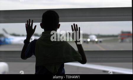 boy stands near the window at the airport and looks at the planes, the boy dreams of becoming a pilot, have fun Stock Photo