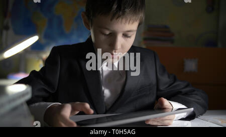 boy in jacket using tablet, doing homework at home, playing at the game Stock Photo