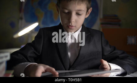 boy in jacket using tablet, doing homework at home, playing at the game Stock Photo